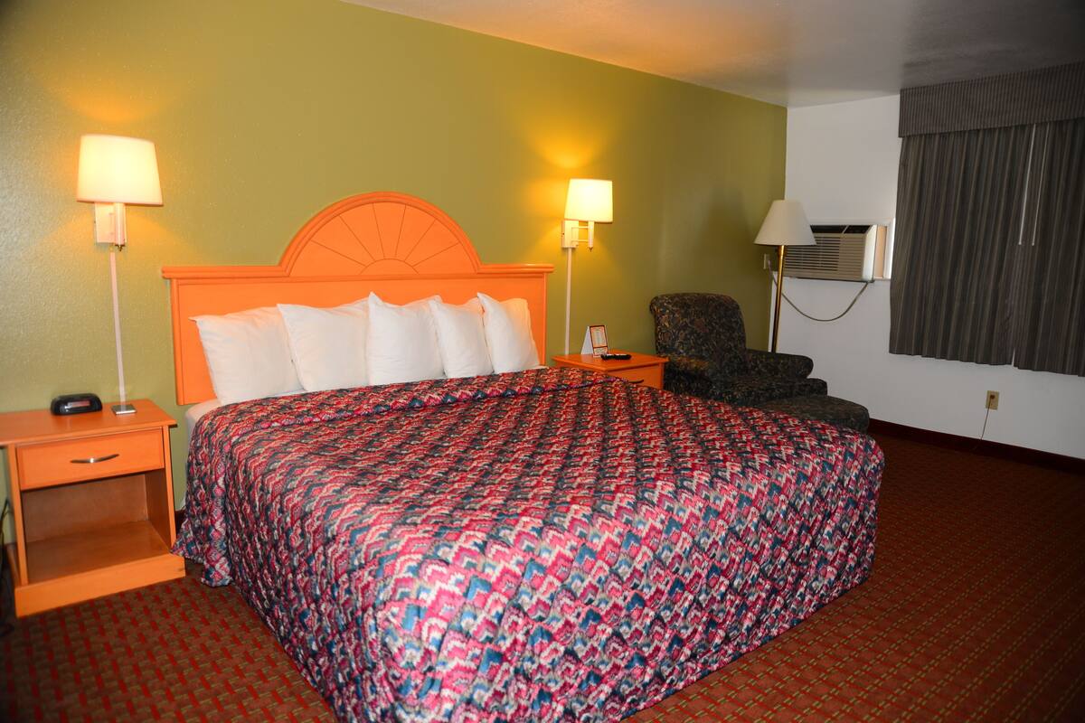 Una habitación de hotel con una cama, dos lámparas de noche, una silla y un equipo de aire acondicionado.