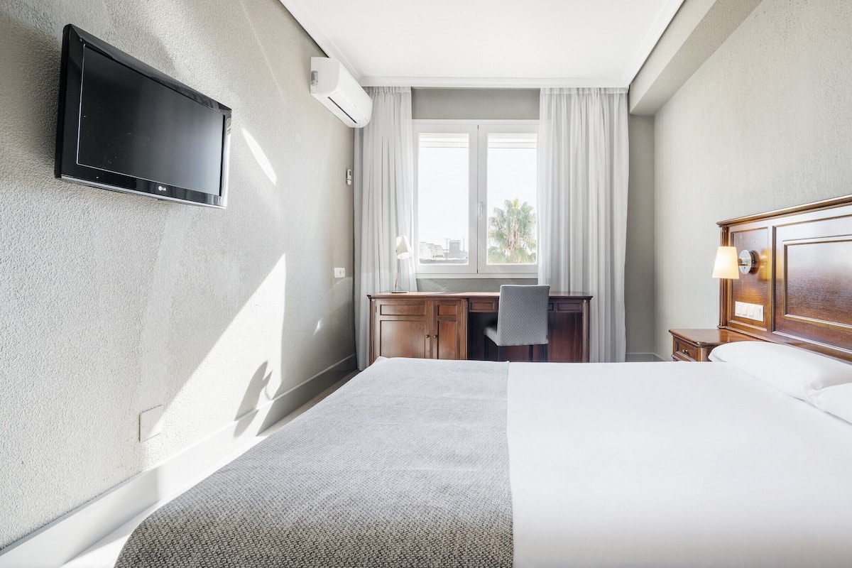 Ein Hotelzimmer mit Bett, Schreibtisch, Stuhl, Fernseher und Klimaanlage.