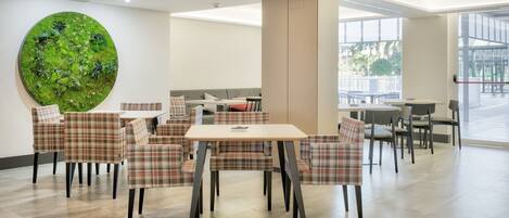 Un comedor moderno con sillas a cuadros, una mesa redonda y una gran obra de arte mural verde.