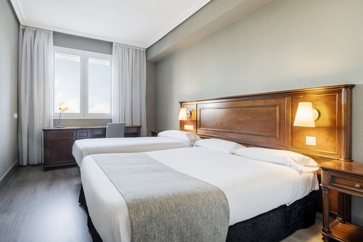 Ein Hotelzimmer mit zwei Betten, einem Schreibtisch, einem Stuhl und einem Fenster mit Vorhängen.