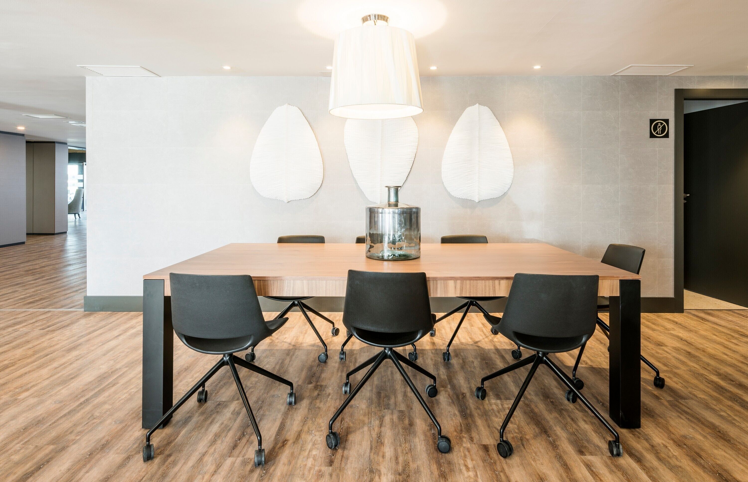 Ein Konferenzraum mit einem großen Tisch, vier schwarzen Stühlen, einer zentralen Lampe und Wanddekoration.