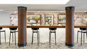 A bar area with a marble floor, black chairs, and a bar counter with shelves of bottles. - Hotel ILUNION Las Lomas (Merida)