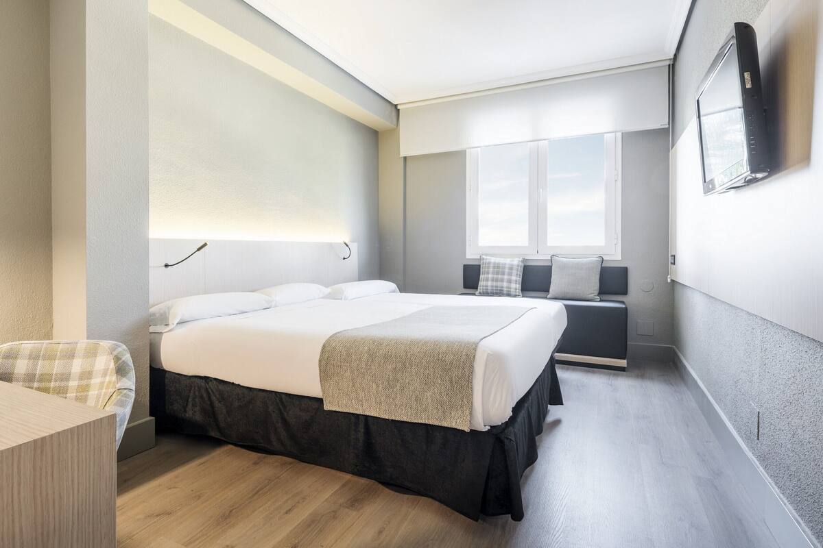 Ein modernes Hotelzimmer mit einem großen Bett, einem Nachttisch, einem Sessel und einem an der Wand befestigten Fernseher.