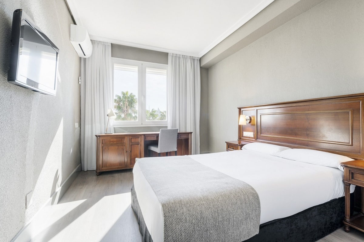 Ein Hotelzimmer mit einem großen Bett, einem Schreibtisch und einem an der Wand befestigten Fernseher.