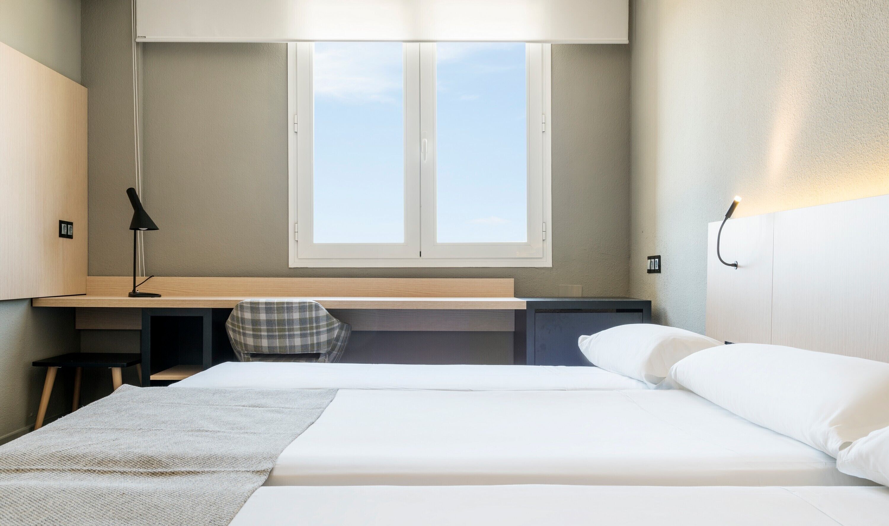 Un dormitorio con una cama, un escritorio, una silla, una ventana y una lámpara de noche.