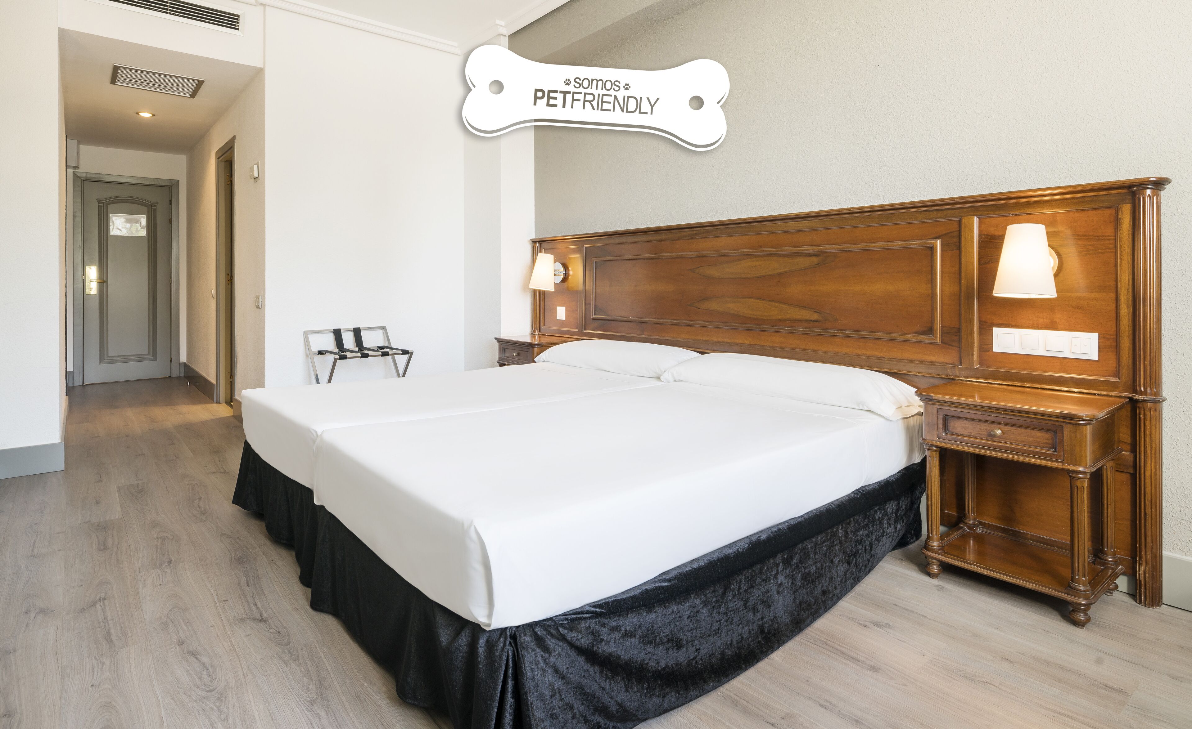 Ein Hotelzimmer mit einem großen Bett, einem hölzernen Kopfteil, Nachttischlampen und einem Schild, das anzeigt, dass Haustiere erlaubt sind.