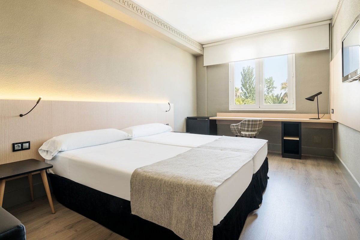 Ein Hotelzimmer mit Bett, Schreibtisch, Stuhl und einem an der Wand befestigten Fernseher.