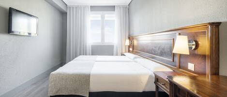 Habitación de hotel con una cama grande, una mesita de noche, un televisor montado en la pared y una ventana con cortinas.