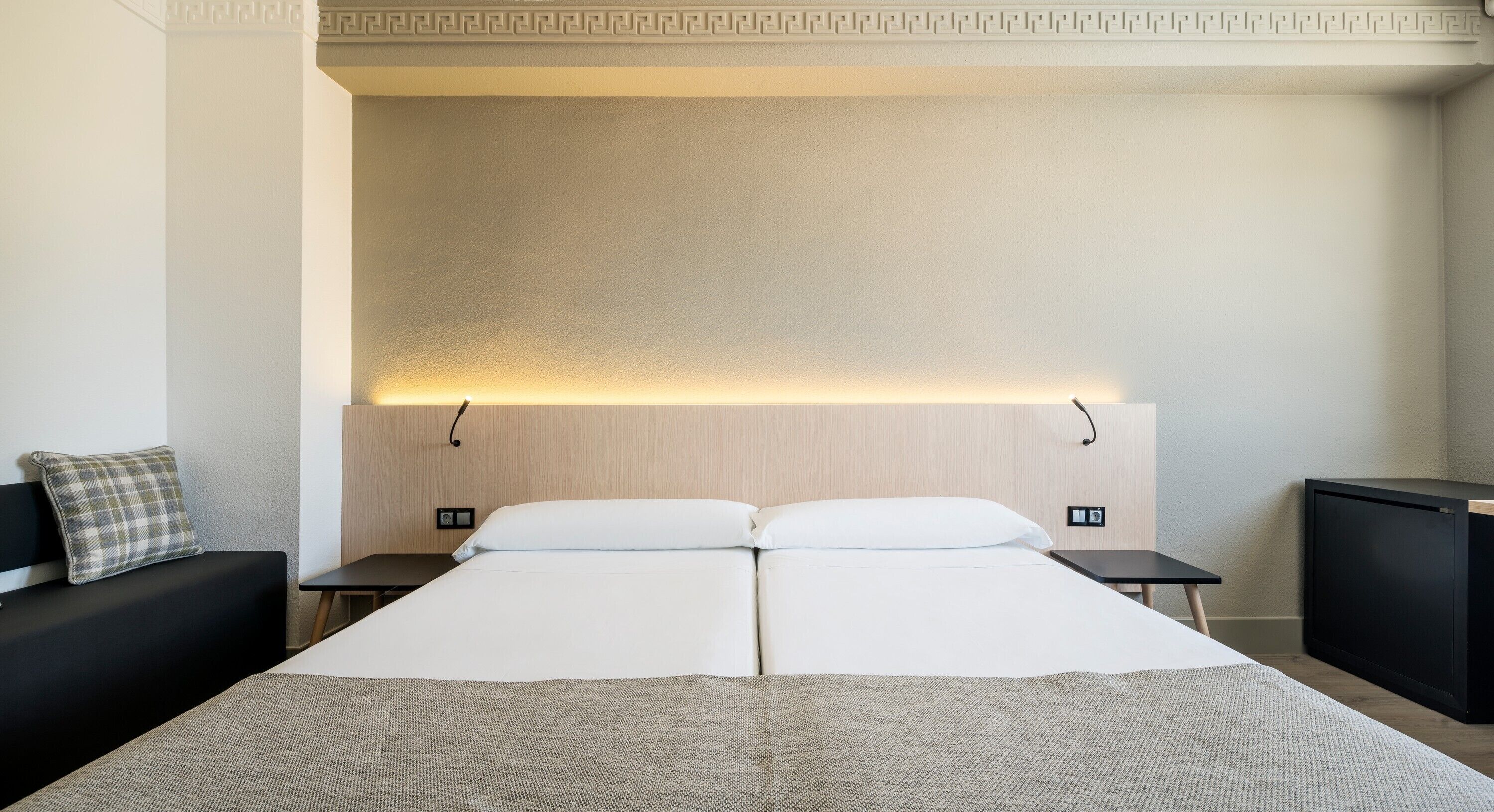 A hotel room with a large bed, two bedside tables, a small TV, and a decorative wall panel.
