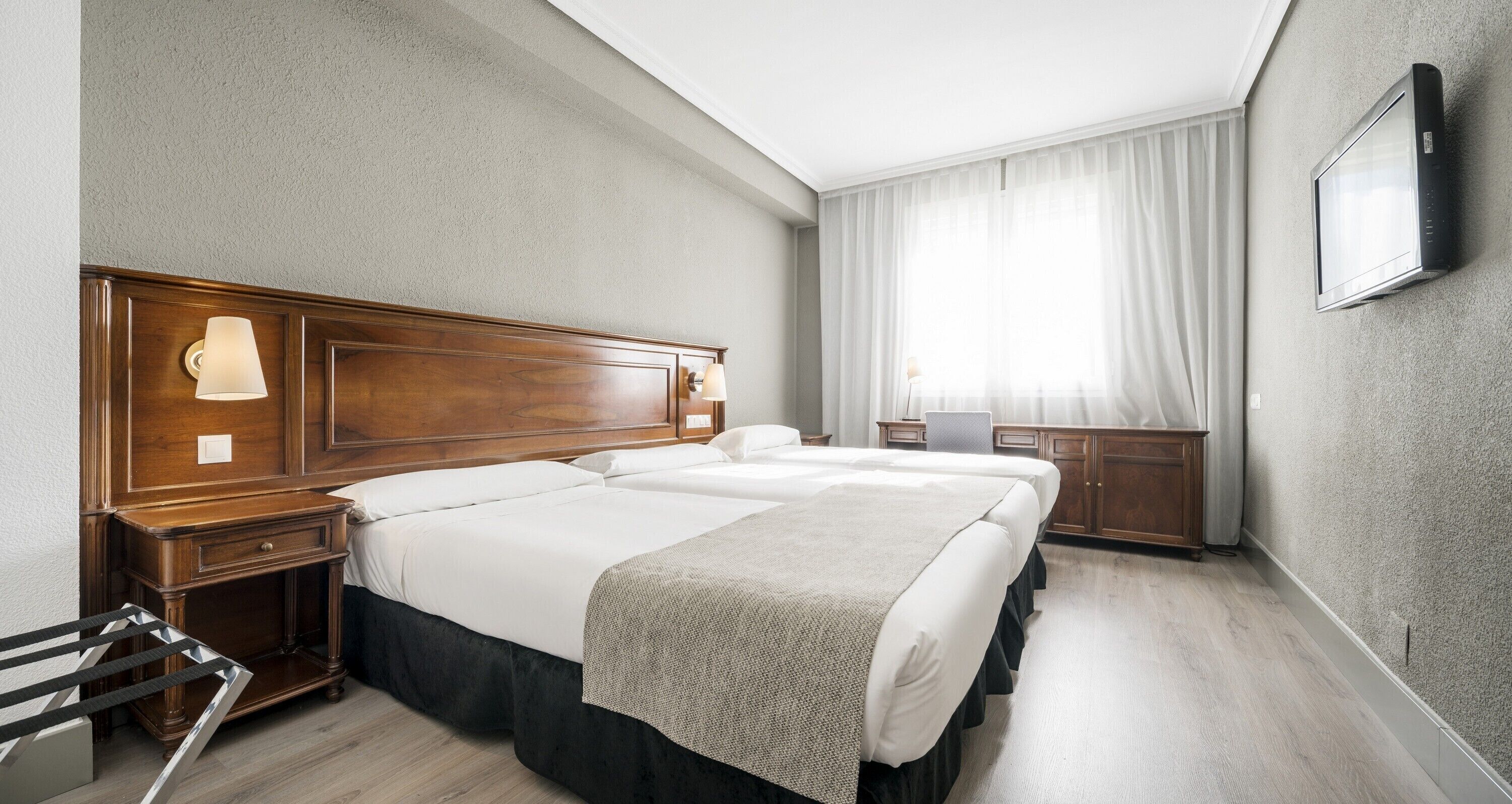 Habitación de hotel con una cama grande, mesitas de noche, un escritorio y un televisor montado en la pared.
