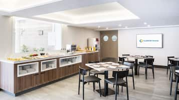 Un área de desayuno moderno en un hotel, con un bufé, mesas para comer y una estación de café.