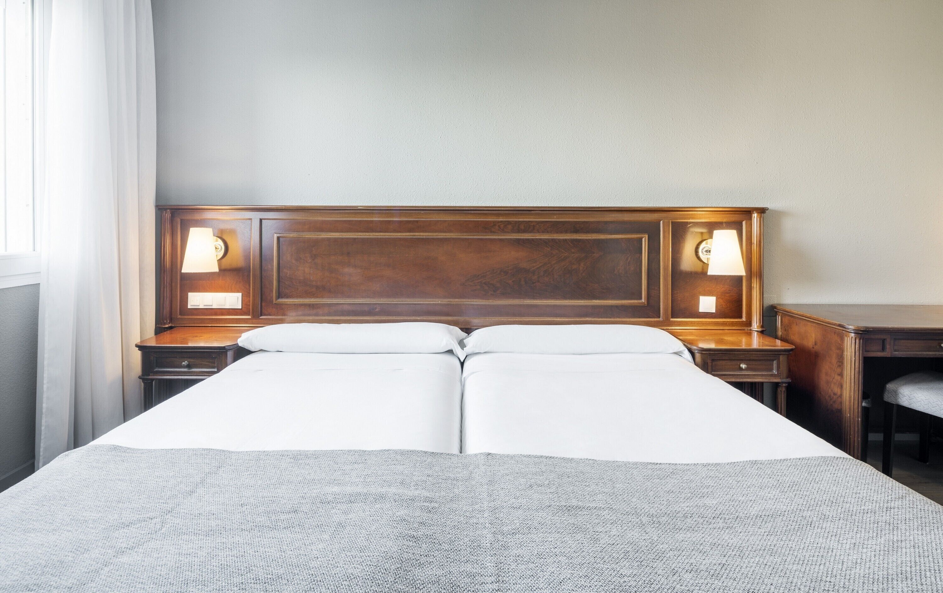 A double bed with a wooden headboard, two bedside tables with lamps, and a plain wall.
