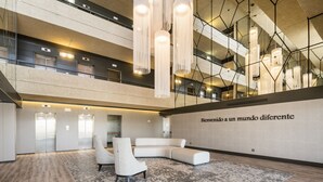 A spacious lobby with a modern design, featuring a large seating area, a high ceiling with hanging lights, and a wall with a welcoming message. - Hotel ILUNION Las Lomas (Merida)