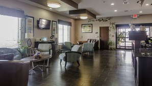 A modern hotel lobby with dark wood flooring, comfortable seating, a flat-screen TV, and a reception desk. - Red River Inn And Suites (Thackerville)