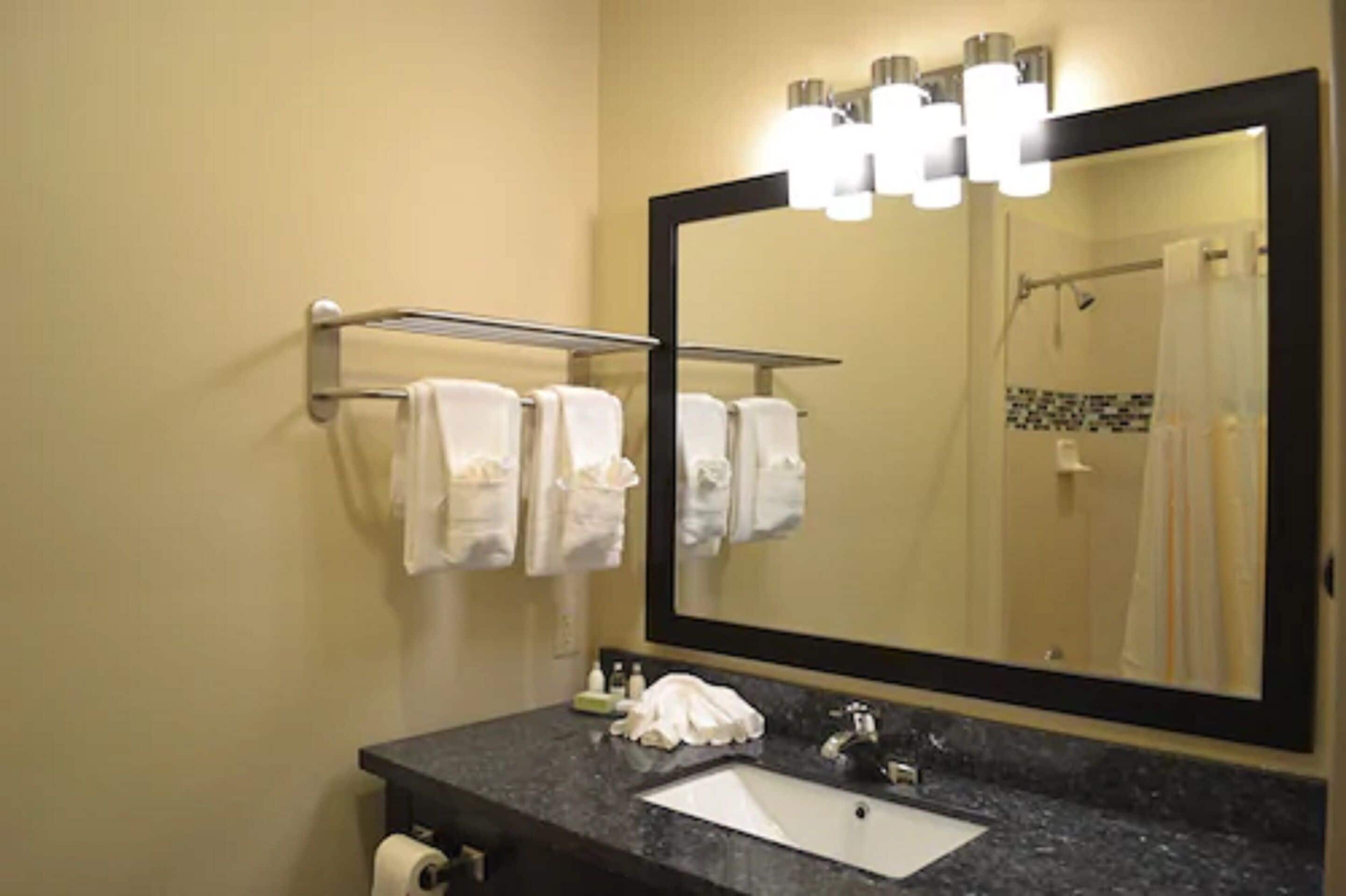 A bathroom with a large mirror, a sink, and a towel rack with multiple towels.