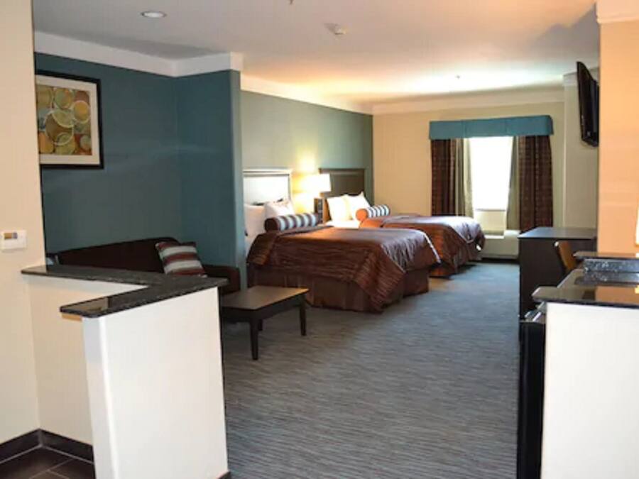 A hotel room with two beds, a desk, a chair, a small table, and a TV.