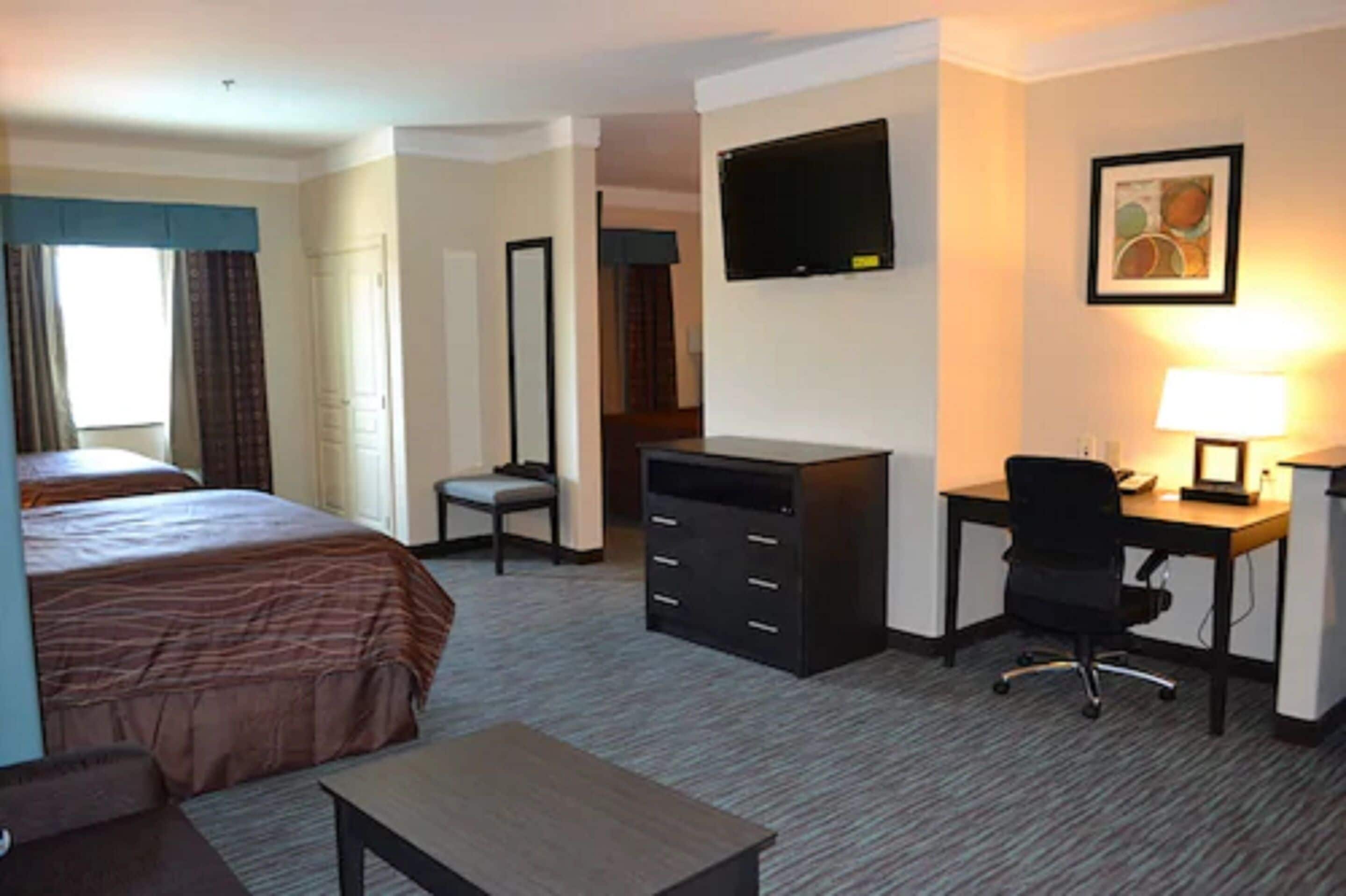 A hotel room with a bed, a desk, a chair, a television, and a lamp.