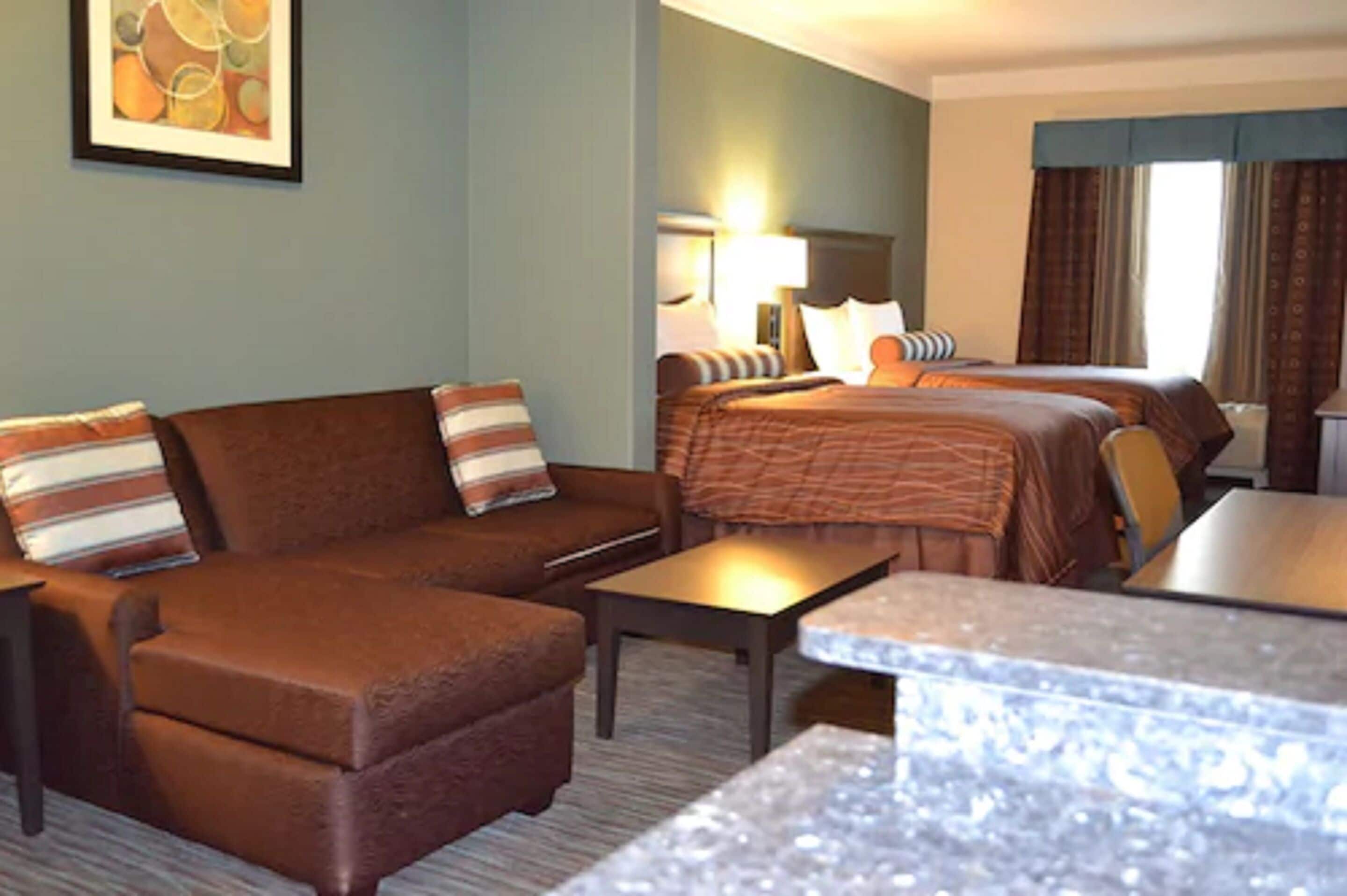 A hotel room with a brown sofa, a bed with a striped blanket, a small table, and a framed picture on the wall.
