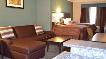 A hotel room with a brown sofa, a bed with a striped blanket, a small table, and a framed picture on the wall.