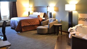A hotel room with a bed, a chair, a small table, and a bathroom with a sink and mirror. - Red River Inn And Suites (Thackerville)
