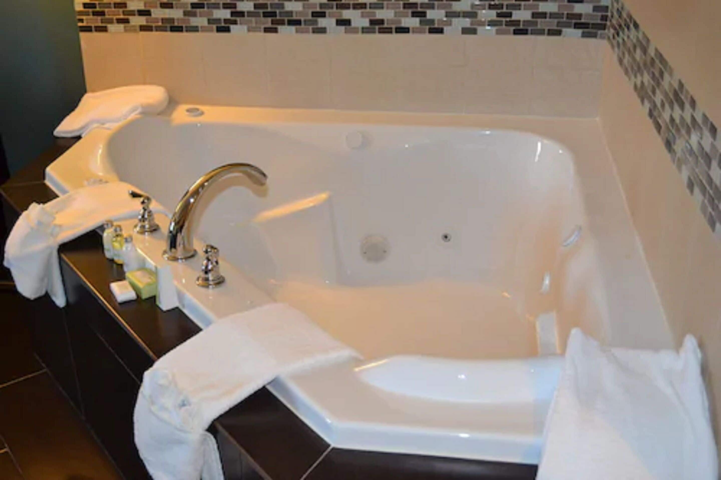 Un baño con una bañera grande, un lavabo y un espejo. Hay toallas y artículos de aseo en la encimera.