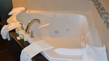 Un baño con una bañera grande, un lavabo y un espejo. Hay toallas y artículos de aseo en la encimera.