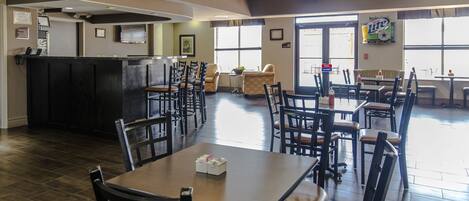 A spacious restaurant with a bar area, multiple tables and chairs, and large windows providing natural light.