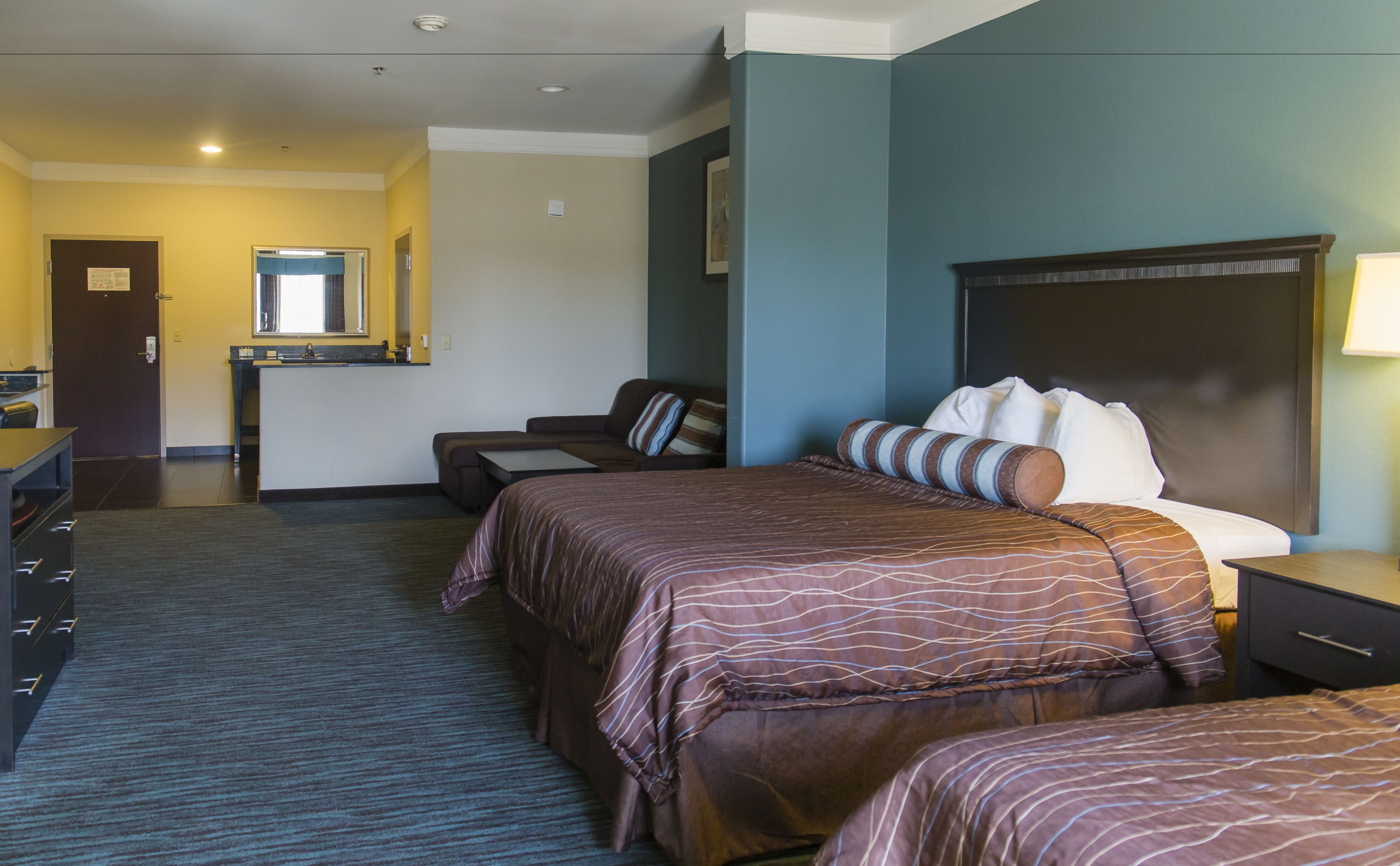 A hotel room with a large bed, a smaller bed, a desk, and a seating area.