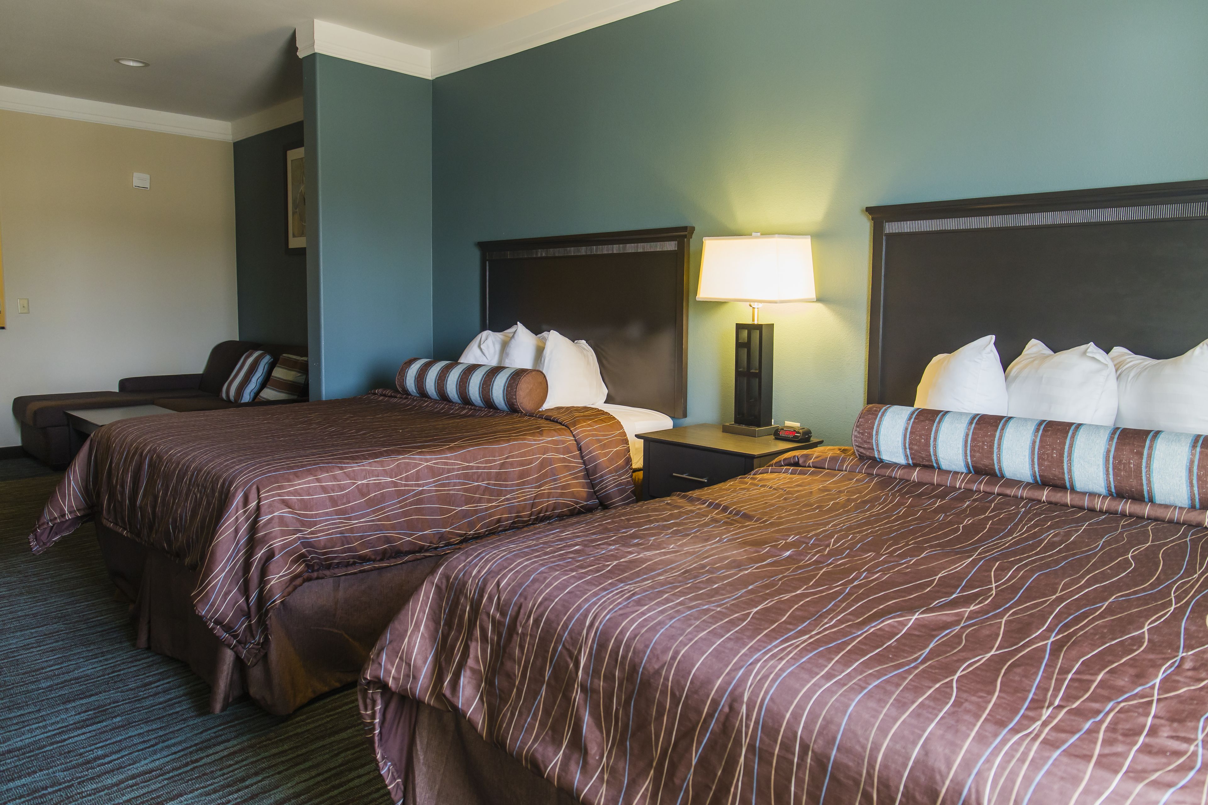 A hotel room with two beds, a desk, a chair, and a nightstand with a lamp.