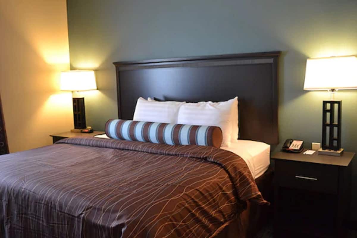 A hotel room with a large bed, two bedside tables with lamps, a nightstand with a phone, and a drawer.