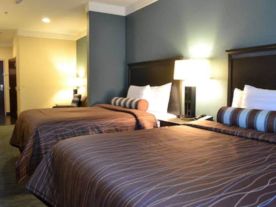 A hotel room with two beds, a nightstand, a lamp, and a door.