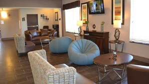 A living room with a sofa, two bean bags, a coffee table, and a TV mounted on the wall. - Red River Inn And Suites (Thackerville)