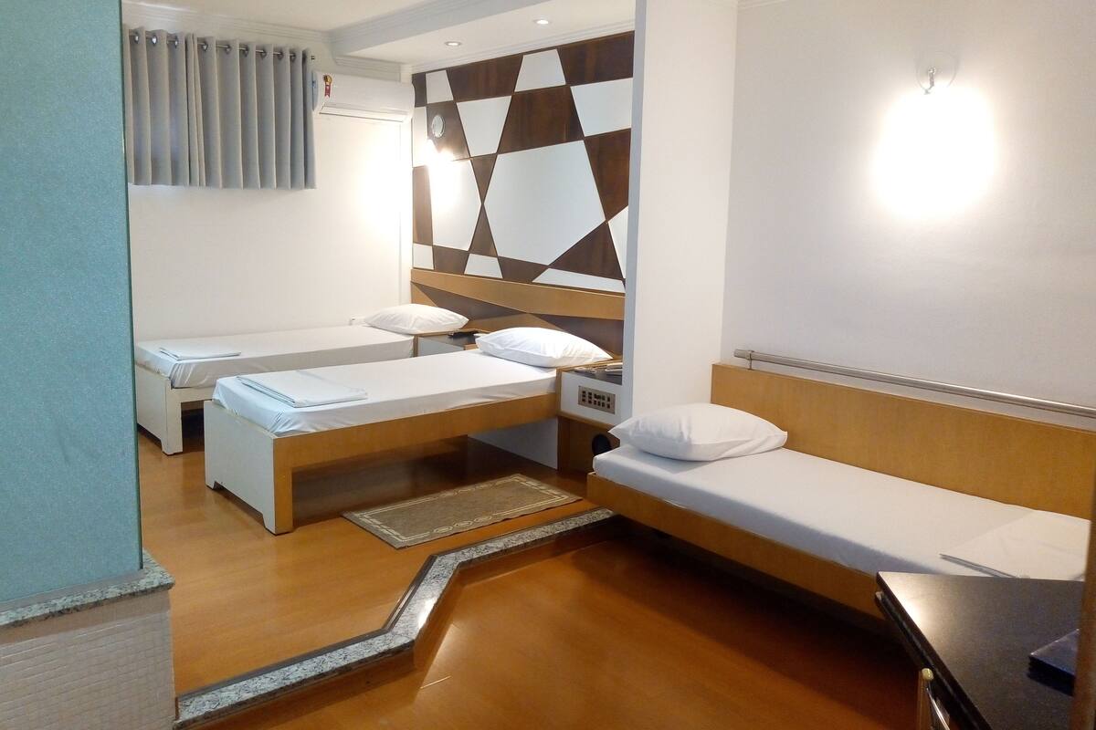 Une chambre d’hôtel avec deux lits simples, une tête de lit en bois, un climatiseur fixé au mur et un motif décoratif sur le mur.