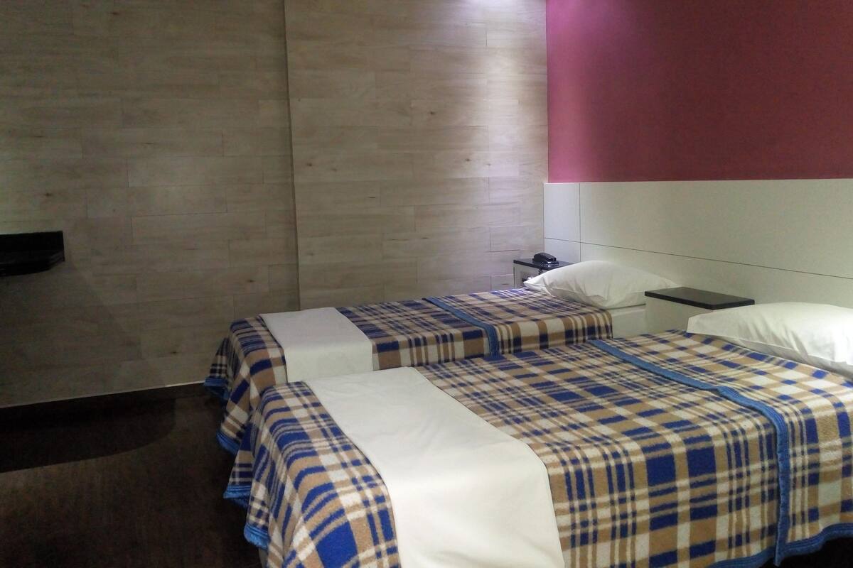 Une chambre d’hôtel avec deux lits, une table de chevet avec une lampe et un téléphone fixé au mur.