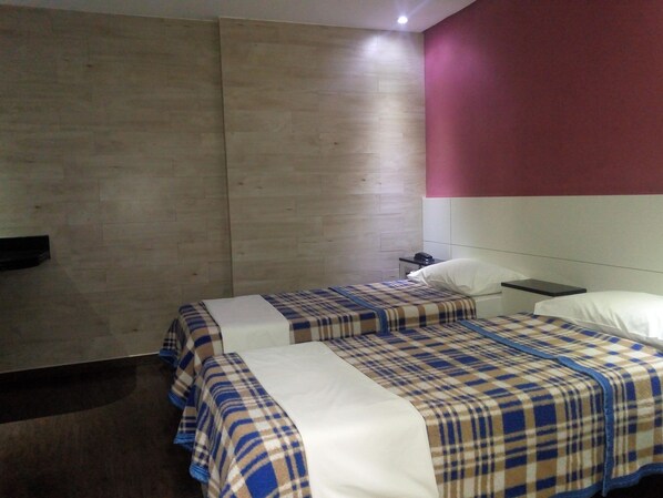 A hotel room with two beds, a bedside table with a lamp, and a wall-mounted telephone.