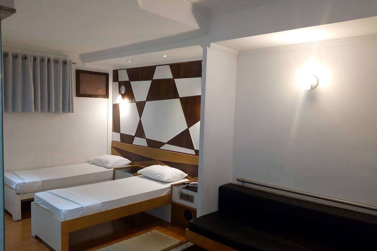 Une chambre avec deux lits simples, un canapé, une tête de lit à motifs géométriques et un luminaire fixé au mur.