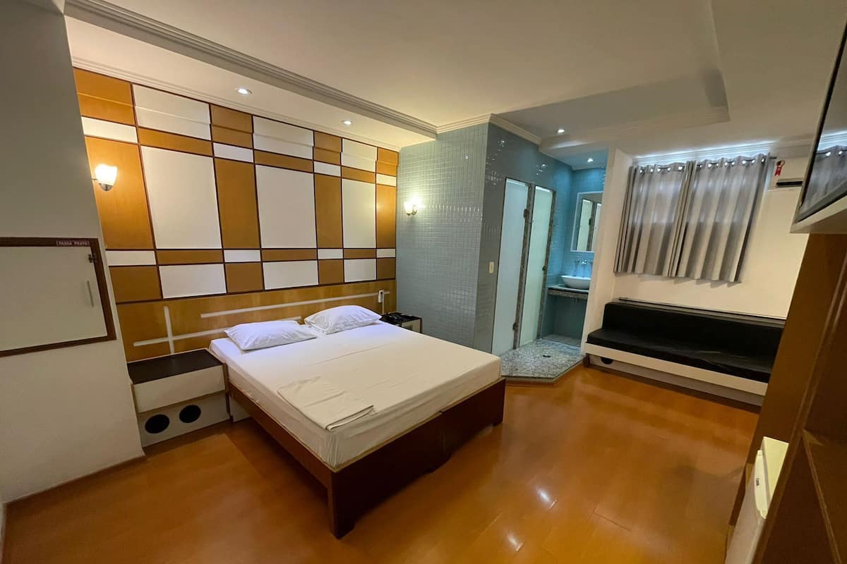Une chambre d’hôtel comprenant un lit, un petit bureau, un miroir, un lavabo et un espace douche.