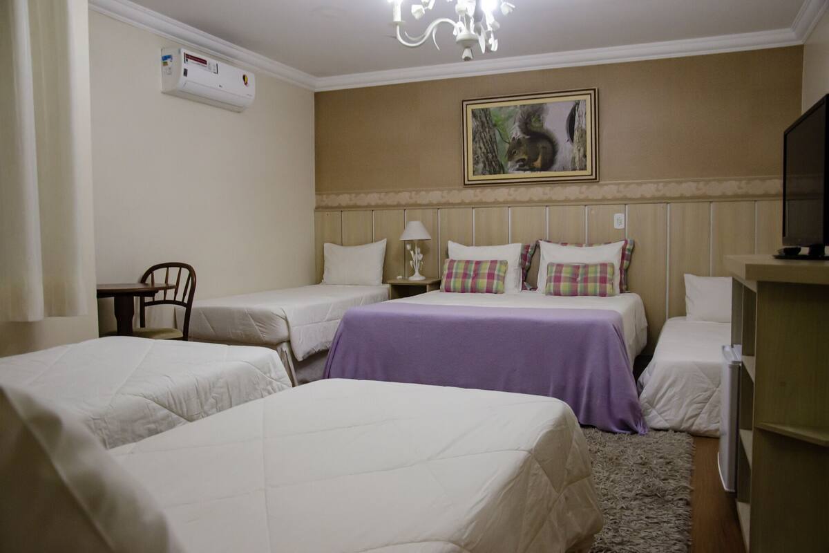 A hotel room with two single beds, a desk with a chair, a television, and a painting on the wall.
