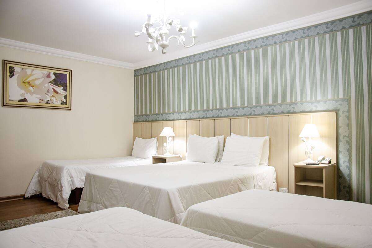 A hotel room with two single beds, a chandelier, a painting on the wall, and striped wallpaper.
