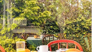 A table set outdoors with a green tablecloth, white cups, a glass of orange juice, and a plate of bread and fruit. - VELINN Pousada Chateau do Luar Prime (Campos do Jordão)
