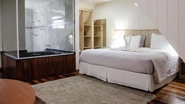 A bedroom with a large bed, a walk-in closet, and a spa-like bathroom with a hot tub. - VELINN Pousada Chateau do Luar Prime (Campos do Jordão)