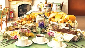 A dining table set with various breads, pastries, and small dishes, with a fireplace and a television in the background. - VELINN Pousada Chateau do Luar Prime (Campos do Jordão)