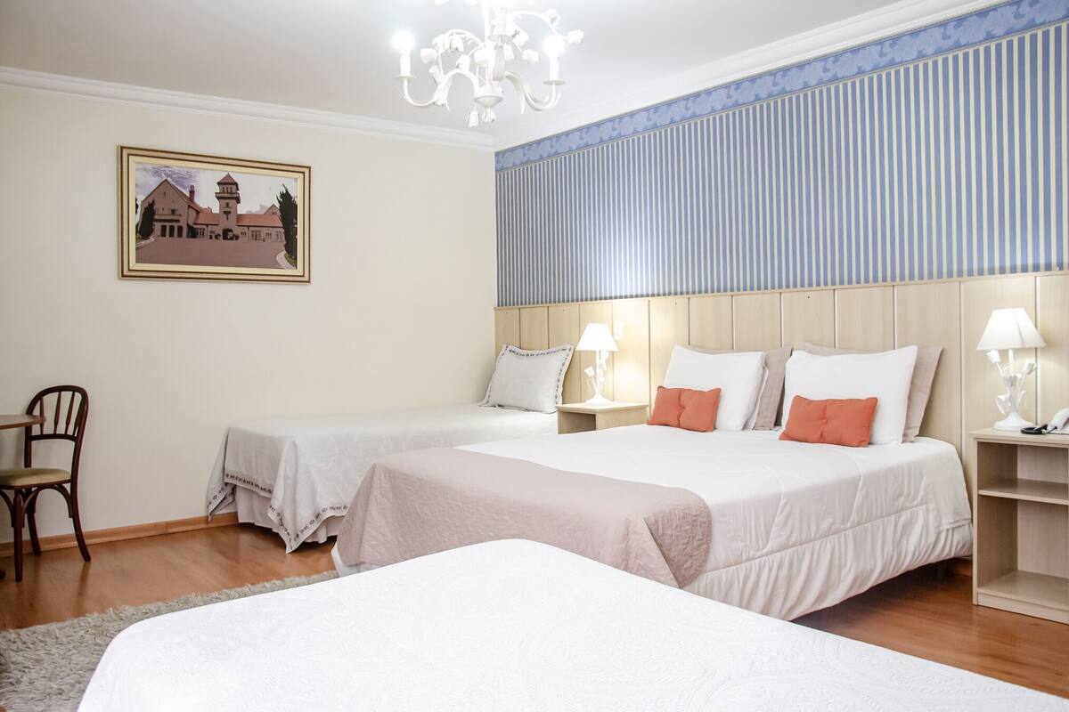 A hotel room with two beds, a wooden headboard, a nightstand with a lamp, a chair, and a framed picture on the wall.