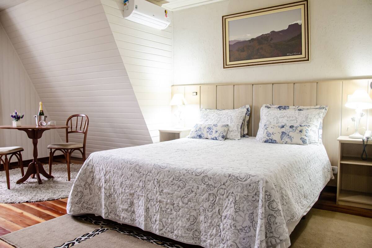 A bedroom with a large bed, a wooden headboard, a small table with chairs, and a nightstand with a lamp.