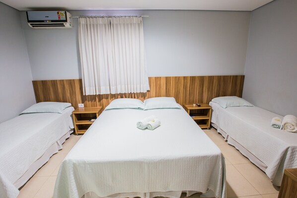 Habitación de hotel con dos camas individuales, cabecero de madera, un ventanal grande con cortinas blancas y un equipo de aire acondicionado.