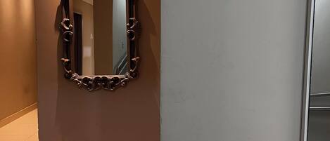A hallway with a large ornate mirror on the left, a sign indicating room numbers, and a door to the right.