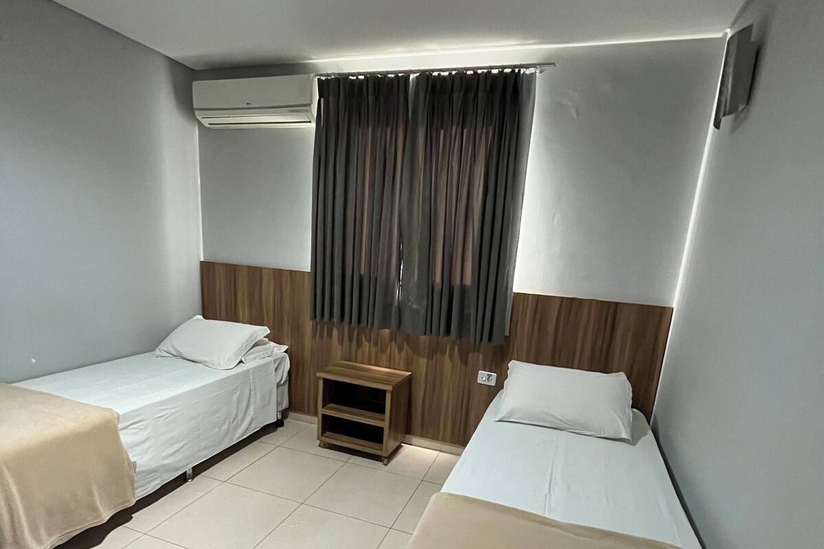 Ein Hotelzimmer mit zwei Einzelbetten, einem kleinen Nachttisch und einem Fenster mit Vorhängen.