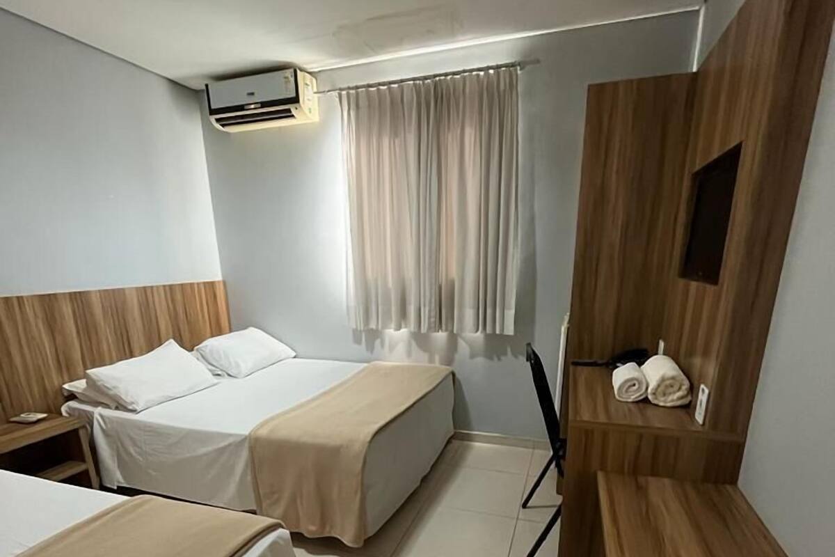 Ein Hotelzimmer mit zwei Betten, einem Schreibtisch, einem Stuhl, einem Kleiderschrank und einem Fenster mit Vorhängen.
