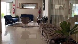 A modern hotel lobby with a plush sofa, a blue armchair, a potted plant, and a large mirror on the wall. - Maximus Sottile Hotel (Ji Parana)