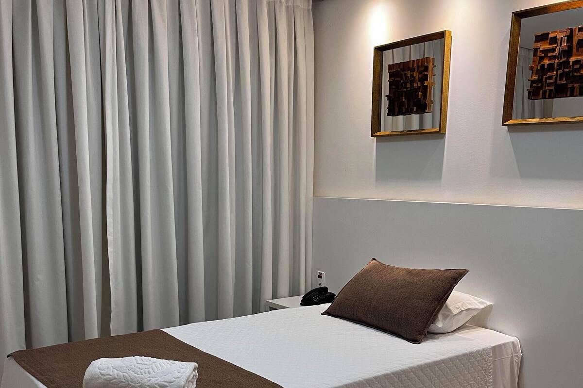 Ein Hotelzimmer mit Bett, Nachttisch, Telefon und einem an der Wand hängenden Kunstwerk.